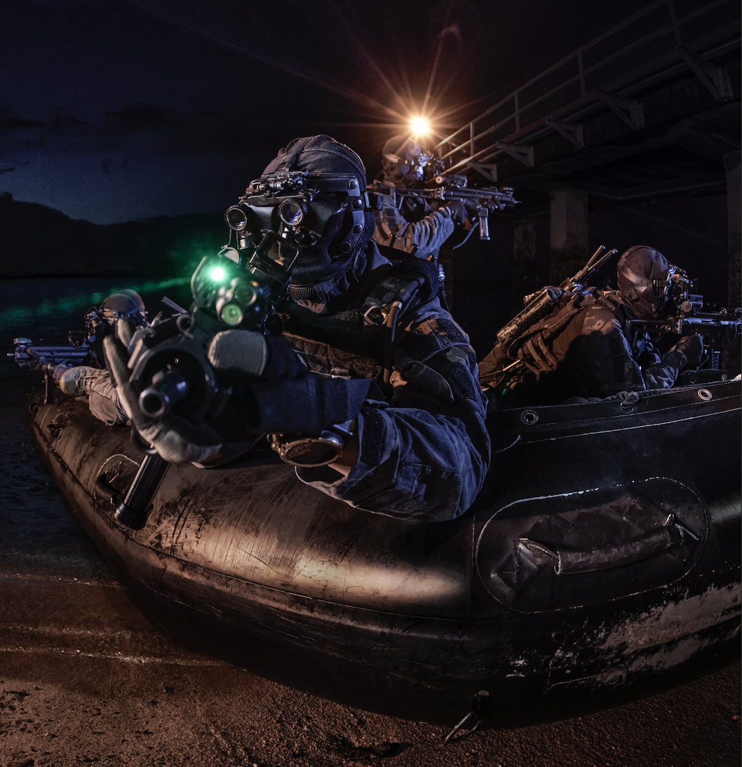 Naval divers in tactical gear, emerging from a rigid inflatable boat at night